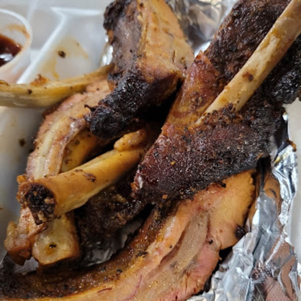 Close-up of Bama Boys BBQ ribs with dark, crispy bark and visible bones, served in foil.