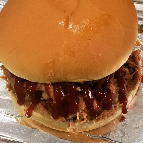 A Bama Boys BBQ pulled pork sandwich, generously topped with barbecue sauce, on a bun.